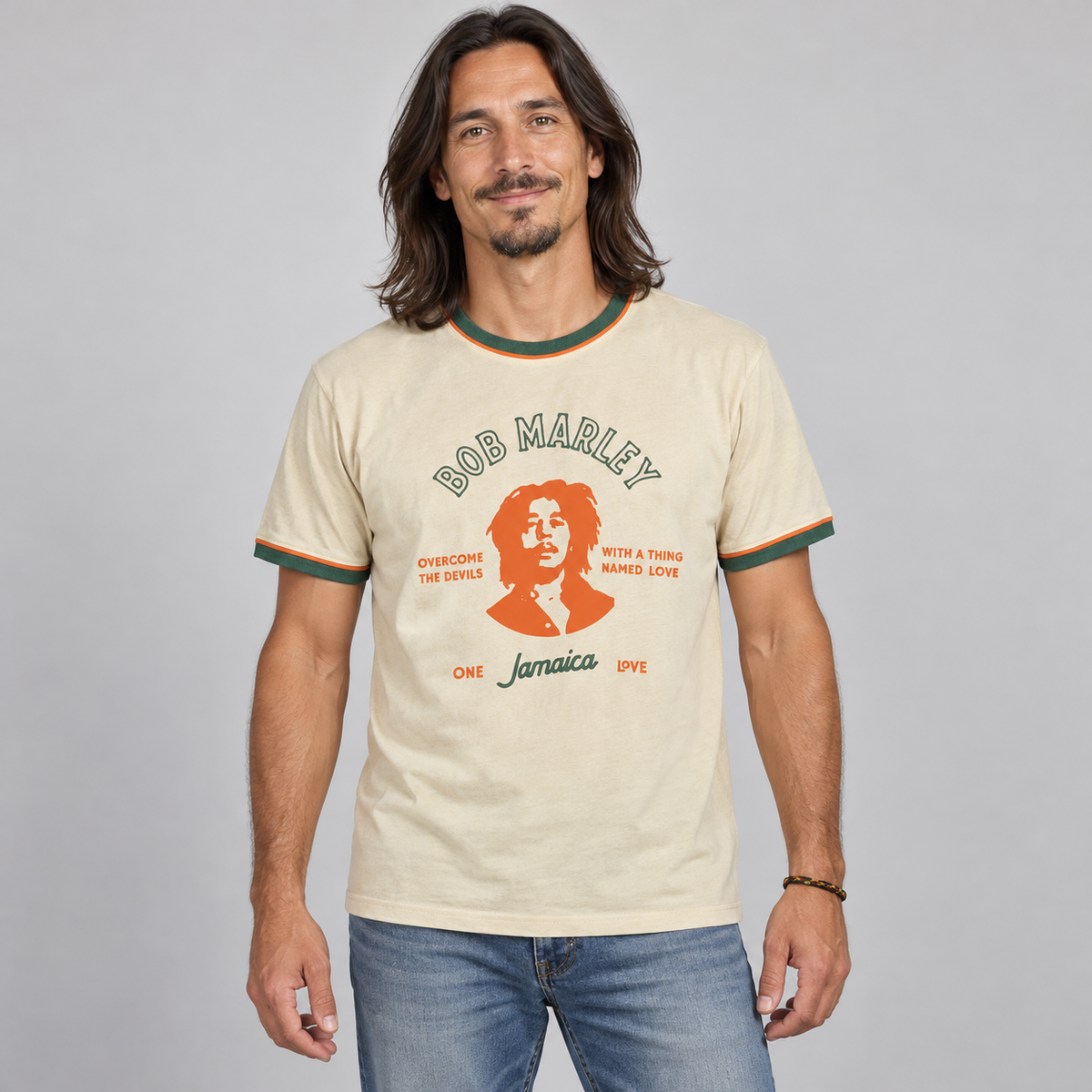 Man wearing the cream Bob Marley Thing Called Loved unisex ringer T-shirt with green and orange trim, studio photo.