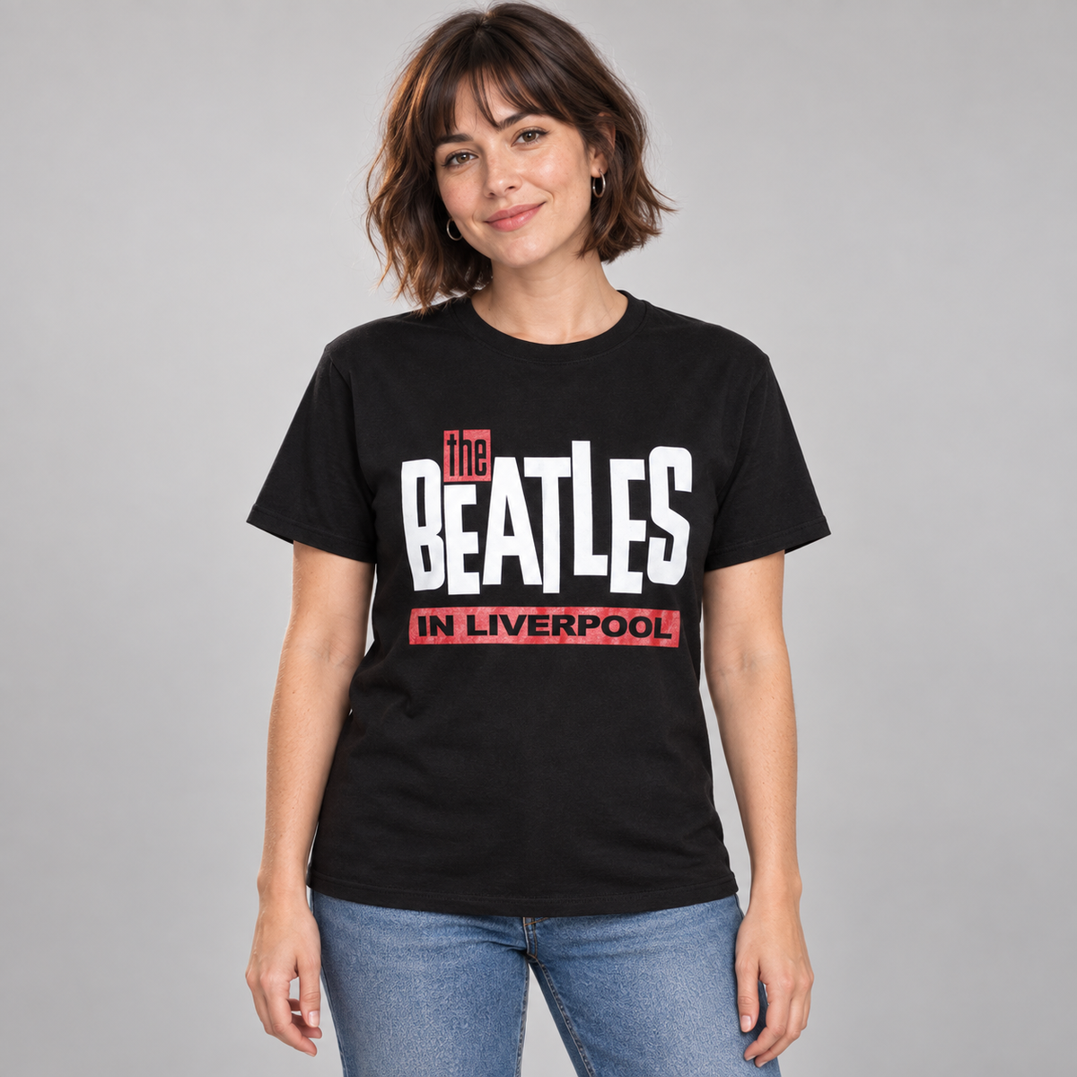 Woman wearing the black Beatles In Liverpool T-shirt with white lettering and red panels in a studio.