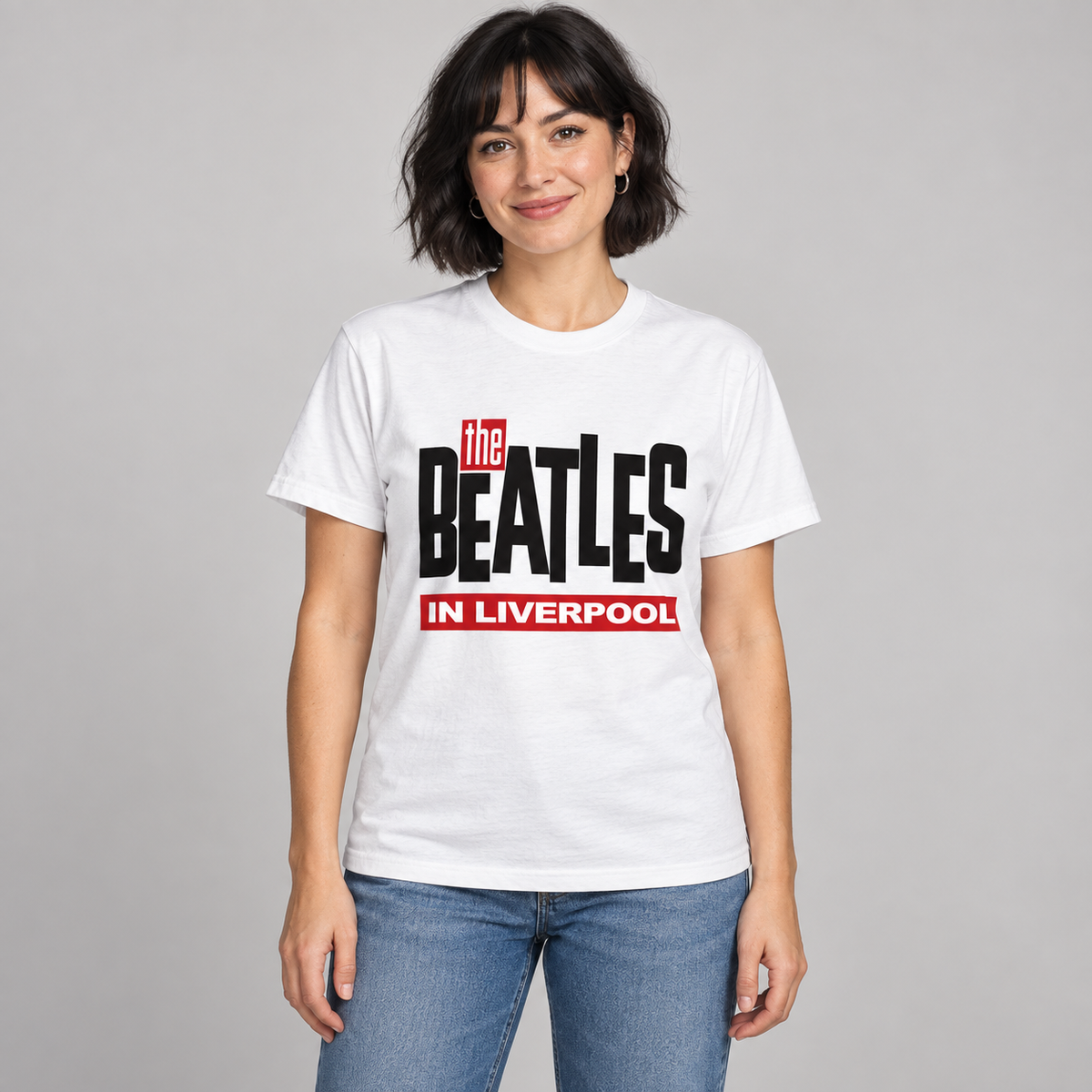 Woman wearing the white The Beatles in Liverpool T-shirt with black and red lettering in a studio.